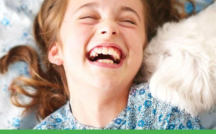 Una niña riendose mientras sus perro blanco le besa en la mejilla