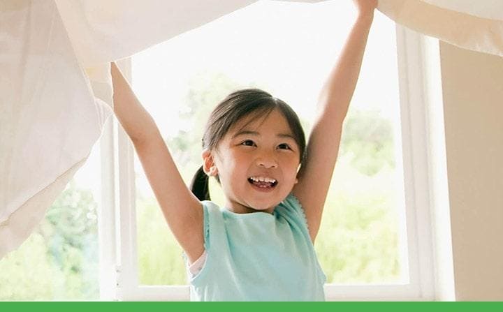 Young girl smiling and raising her arms in front of an open window with  flowing curtains