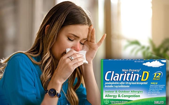 Woman blowing nose into a tissue with Claritin-D package in foreground