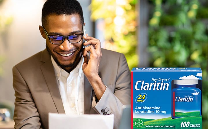 Man smiling on phone with Claritin package in foreground